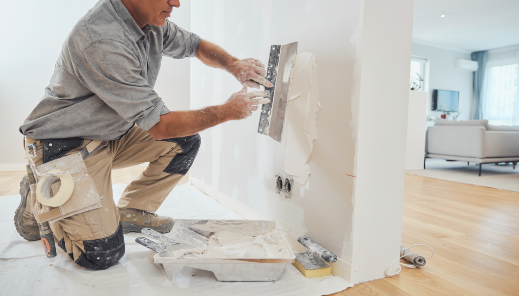 Drywall repair technician patching and smoothing an interior wall in a residential home